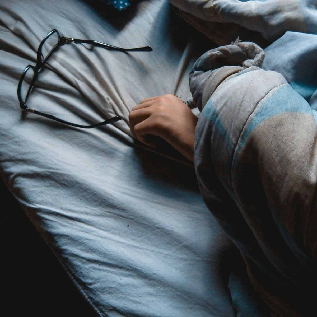 Glasses lying on a bed with outstretched hand.