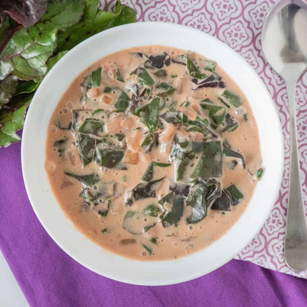 Overhead picture of a bowl of braised greens in a light pink broth.