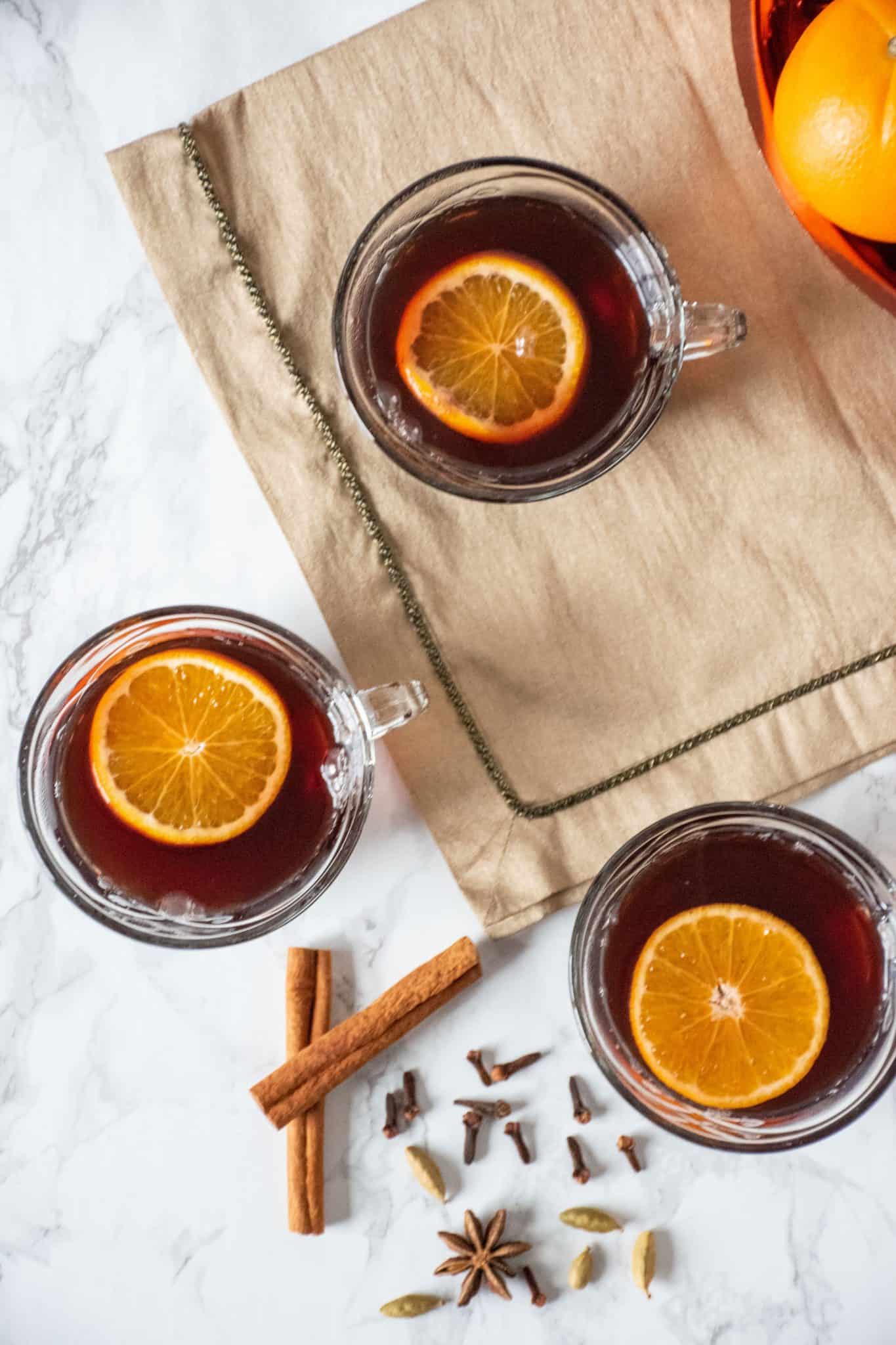 Overhead shot of 3 small glass mugs filled with mulled grape juice, each with an orange slice in them.
