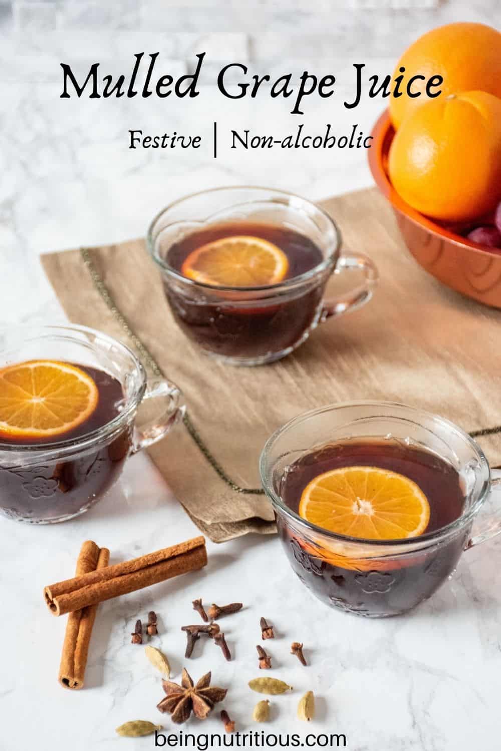 3 small glass mugs filled with mulled grape juice, each with an orange slice in them. Text overlay: Mulled Grape juice; festive; non-alcoholic.