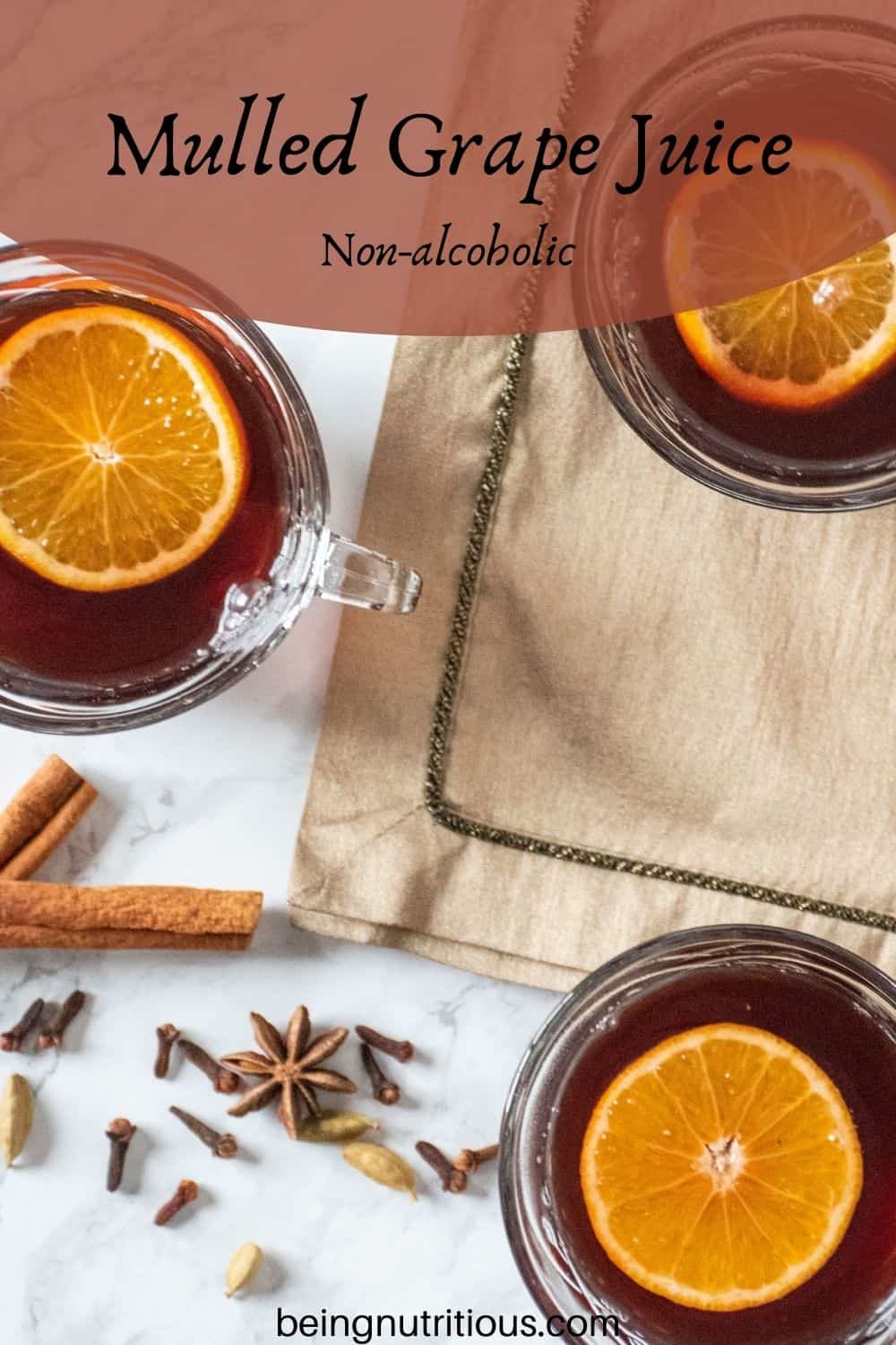 Overhead shot of 3 small glass mugs filled with mulled grape juice, each with an orange slice in them. Text overlay: Mulled Grape Juice; non-alcoholic.