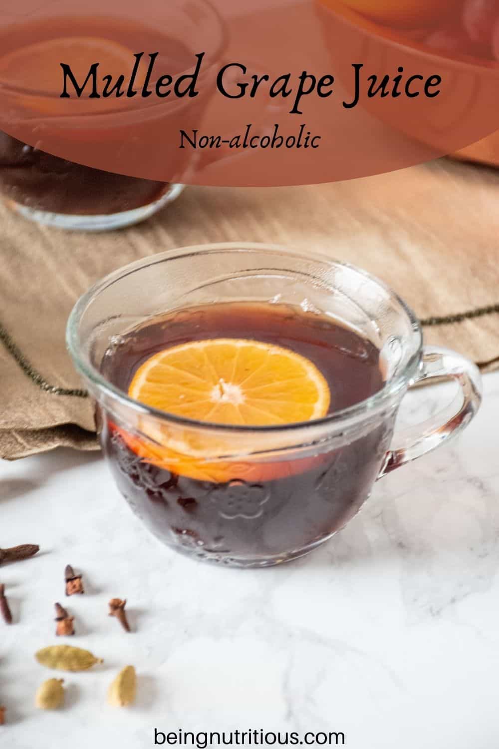 Close up of a small glass mug, filled with mulled grape juice, with an orange slice in it. Text overlay: mulled grape juice; non-alcoholic.