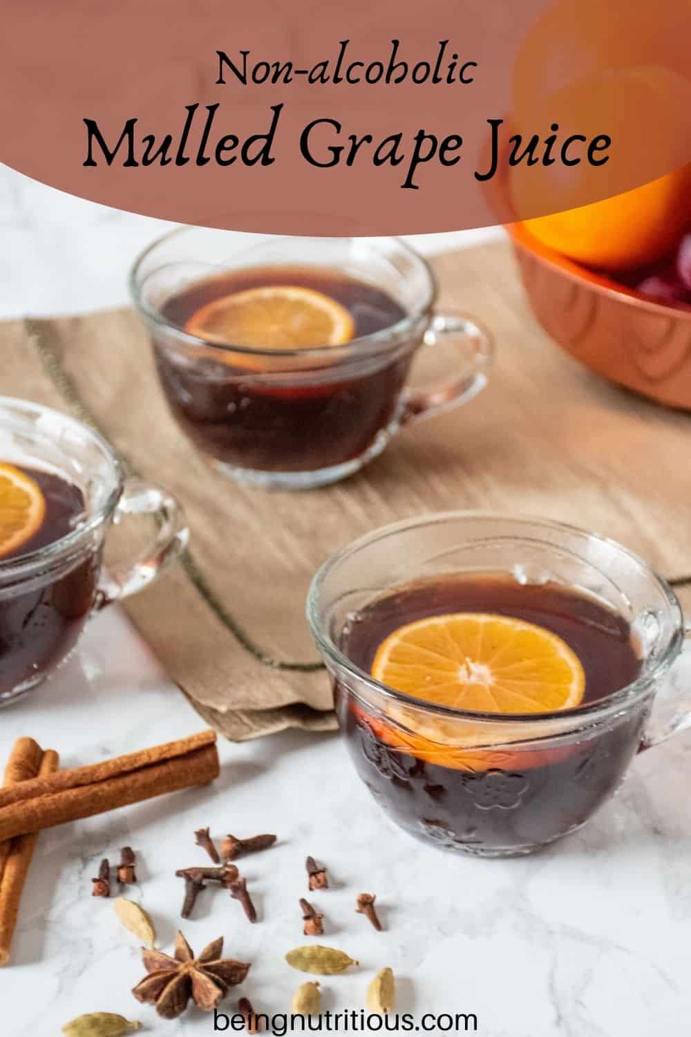 3 small glass mugs filled with mulled grape juice, each with an orange slice in them. Text overlay: Non-alcoholic Mulled Grape juice.