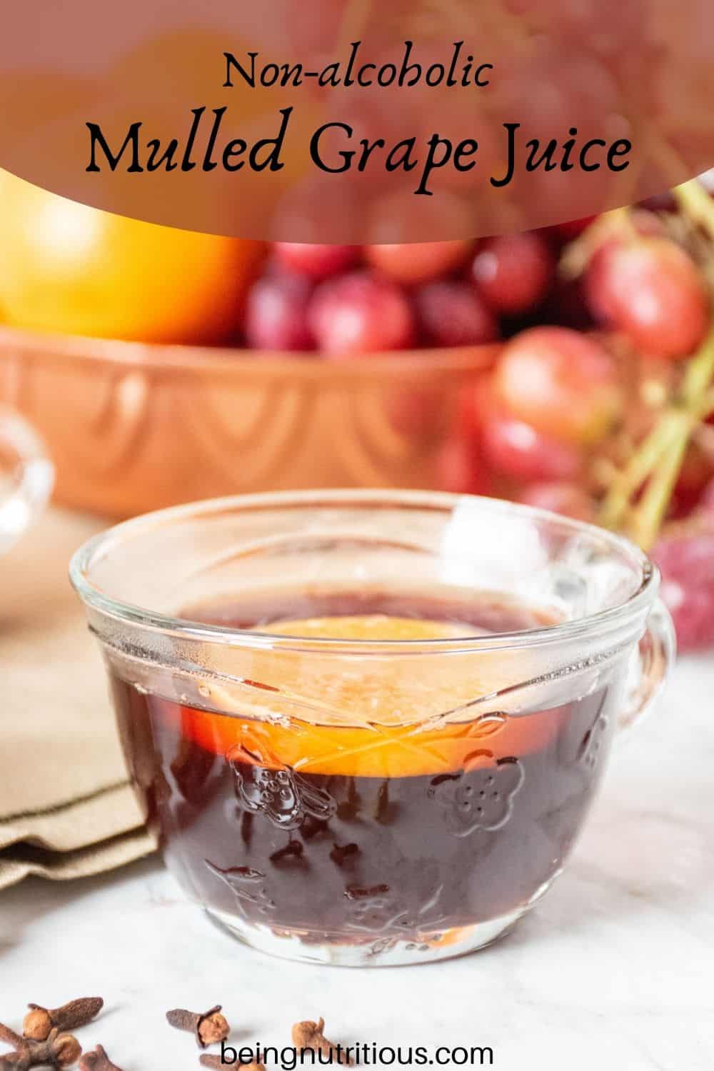 Close up of a small glass mug, filled with mulled grape juice, with an orange slice in it. Text overlay: non-alcoholic mulled grape juice.