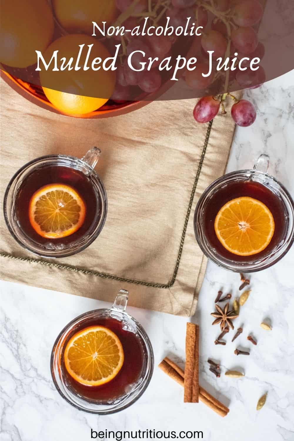 Overhead shot of 3 small glass mugs filled with mulled grape juice, each with an orange slice in them. Text overlay: Non-alcoholic Mulled Grape Juice.