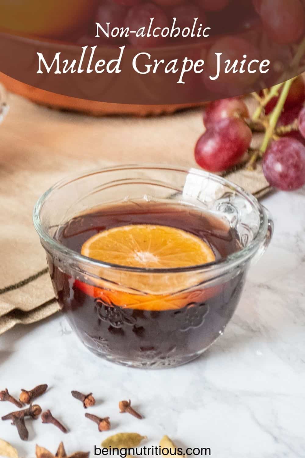 Close up of a small glass mug, filled with mulled grape juice, with an orange slice in it. Text overlay: non-alcoholic mulled grape juice.