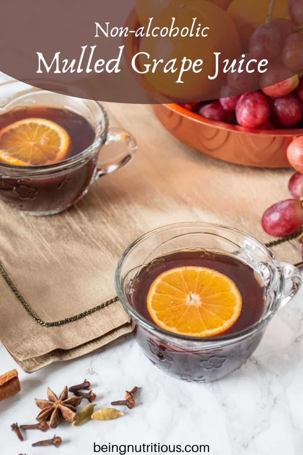 2 small glass mugs filled with mulled grape juice, each with an orange slice in them. Text overlay: Non-alcoholic Mulled Grape juice.