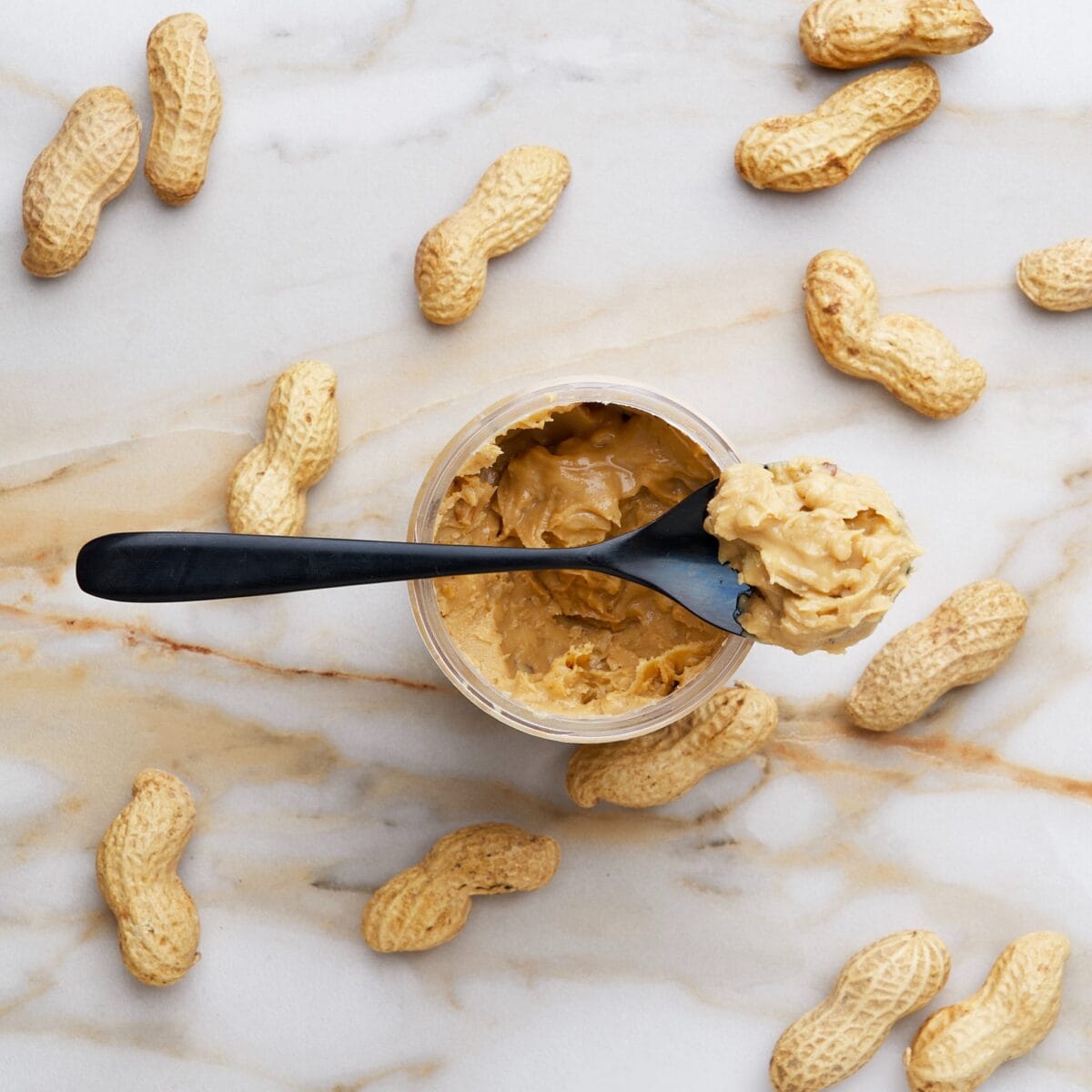 Chunky peanut butter in a jar, surrounded by whole peanuts