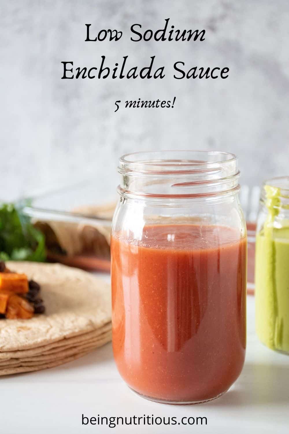 Red sauce in a jar, with enchiladas being made in the background. Text overlay: Low Sodium Enchilada Sauce; 5 minutes!
