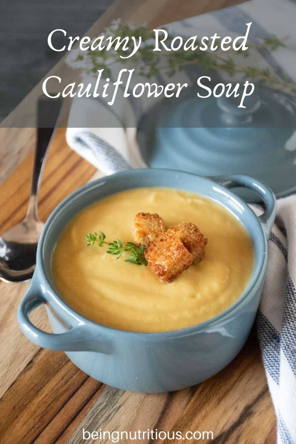 Small bowl of soup with croutons and fresh thyme. Text overlay: Creamy Roasted Cauliflower Soup.