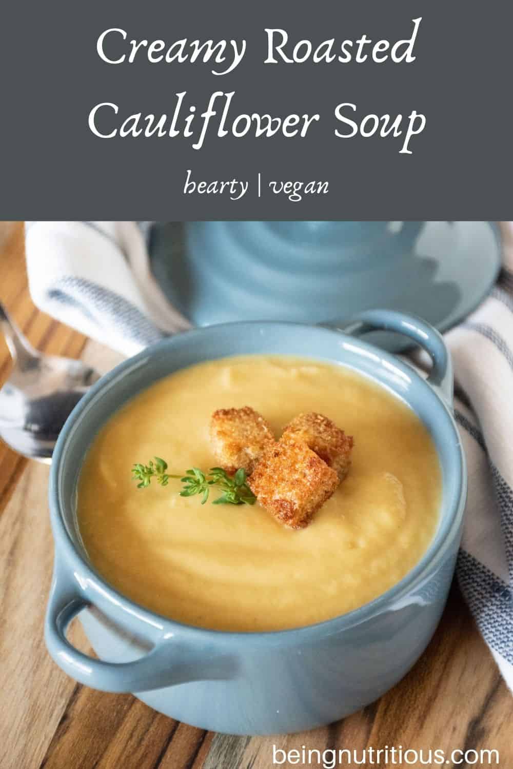 Small bowl of soup with croutons and fresh thyme. Text overlay: Creamy Roasted Cauliflower Soup; hearty, vegan.