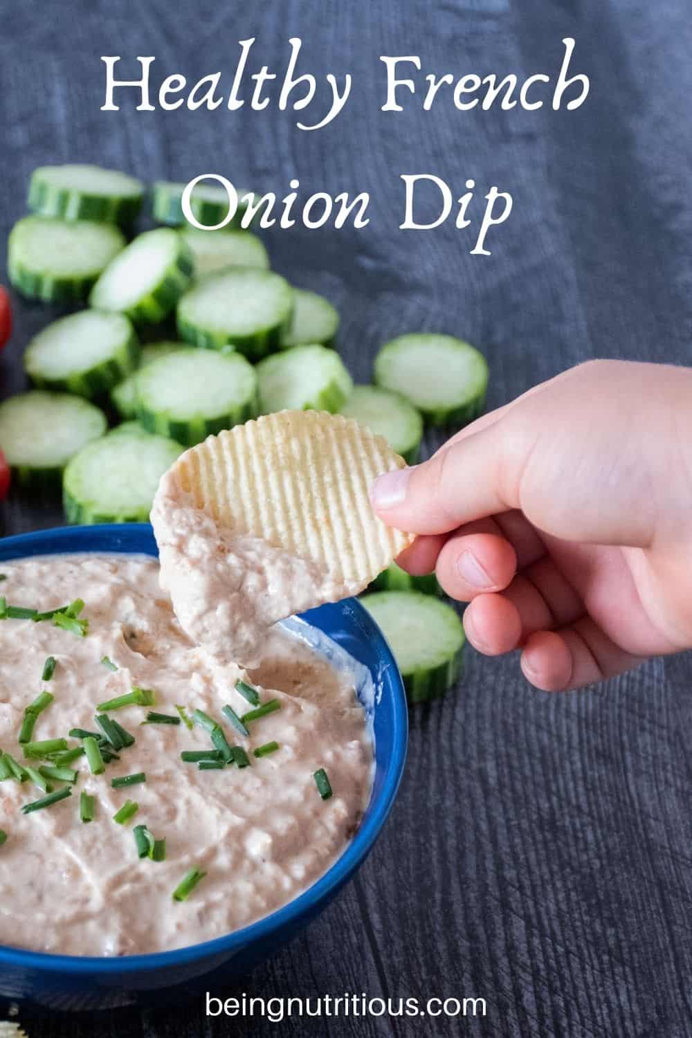 Bowl of dip with cucumber slices in background. Hand holding a chip with dip on it above bowl. Text overlay: Healthy French Onion Dip