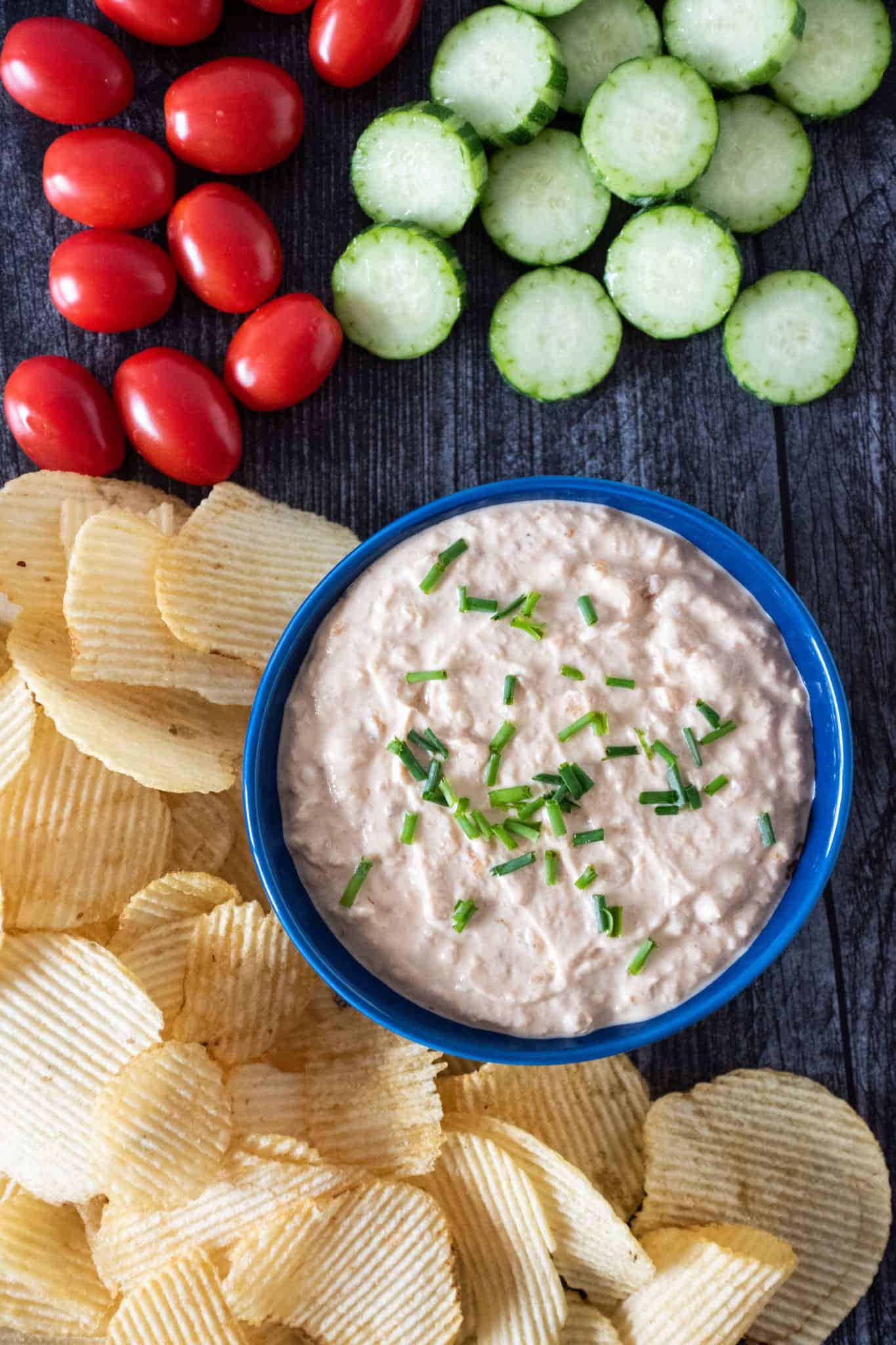 Overhead picture of bowl of dip, surrounded by chips, baby tomatoes, and cucumber slices.