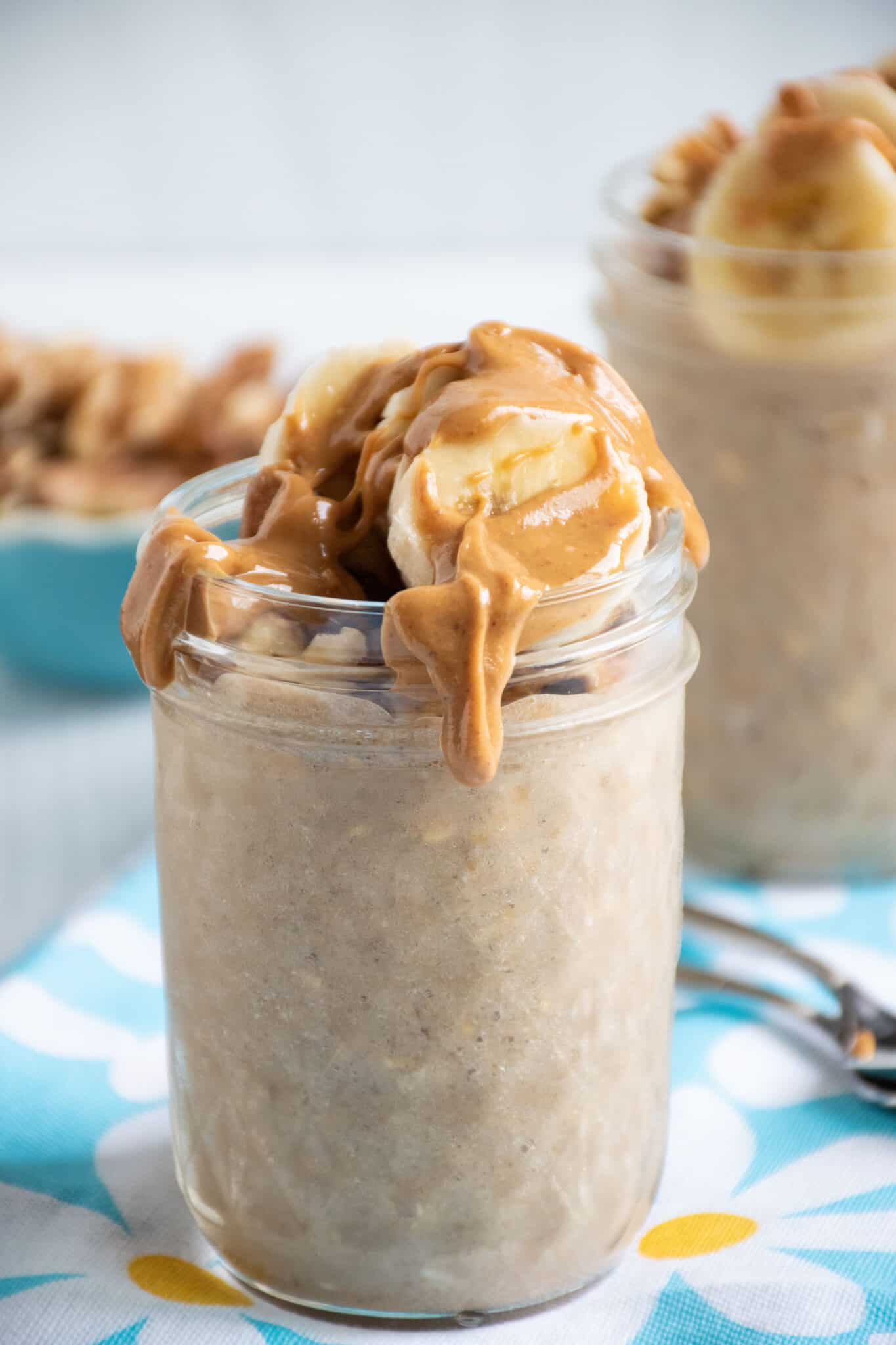 Small mason jar of oatmeal with walnuts and banana slices on top, with a drizzle of peanut butter.