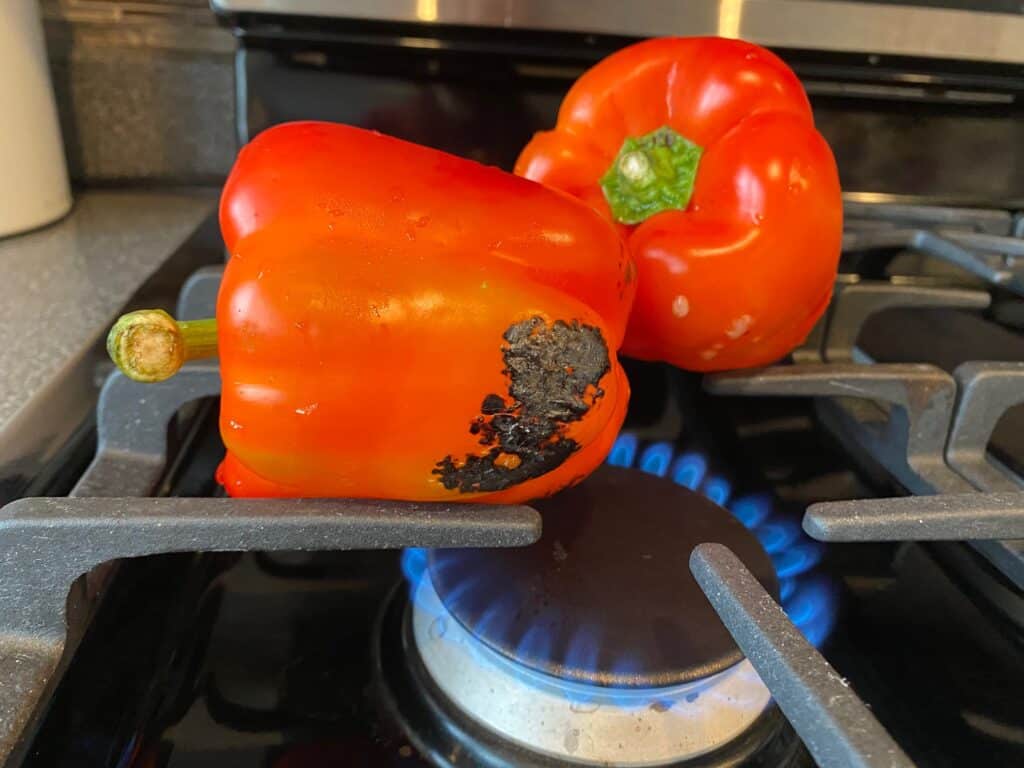 Red peppers starting to char on the stove grate.