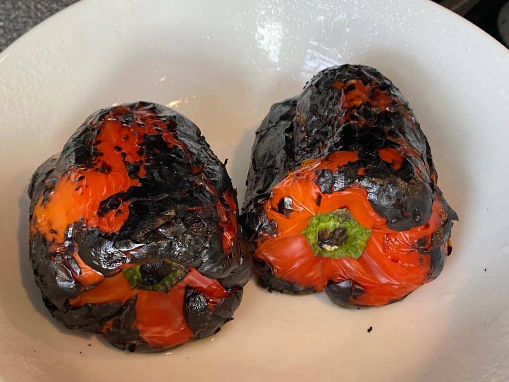 Charred roasted red peppers in a bowl, ready to peel.