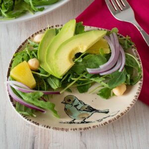 Salad with arugula, avocado, pineapple, red onion, and macadamia nuts on a small serving dish.