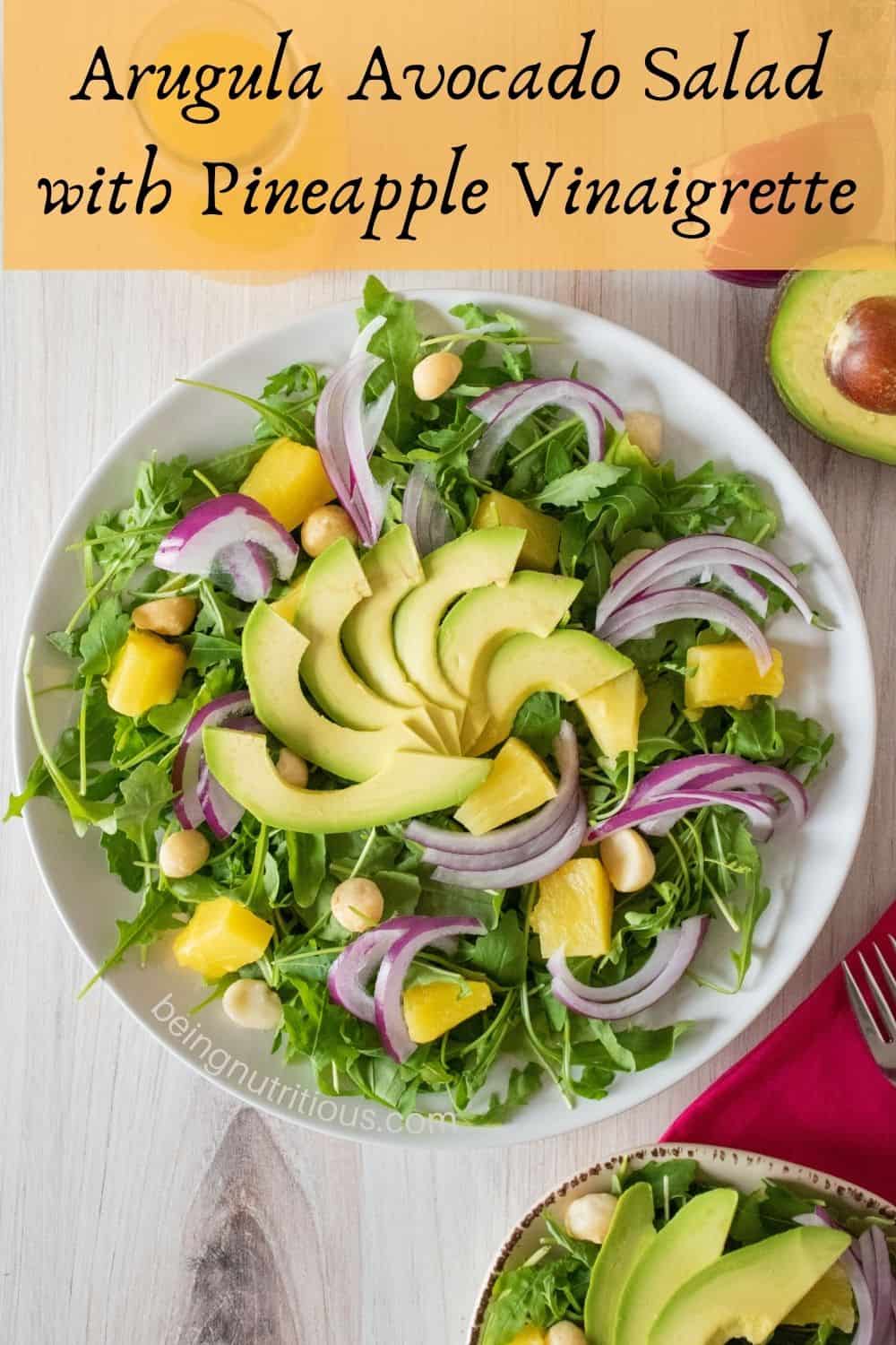 Overhead picture of large plate with salad on it. Text overlay: Arugula Avocado Salad with Pineapple Vinaigrette