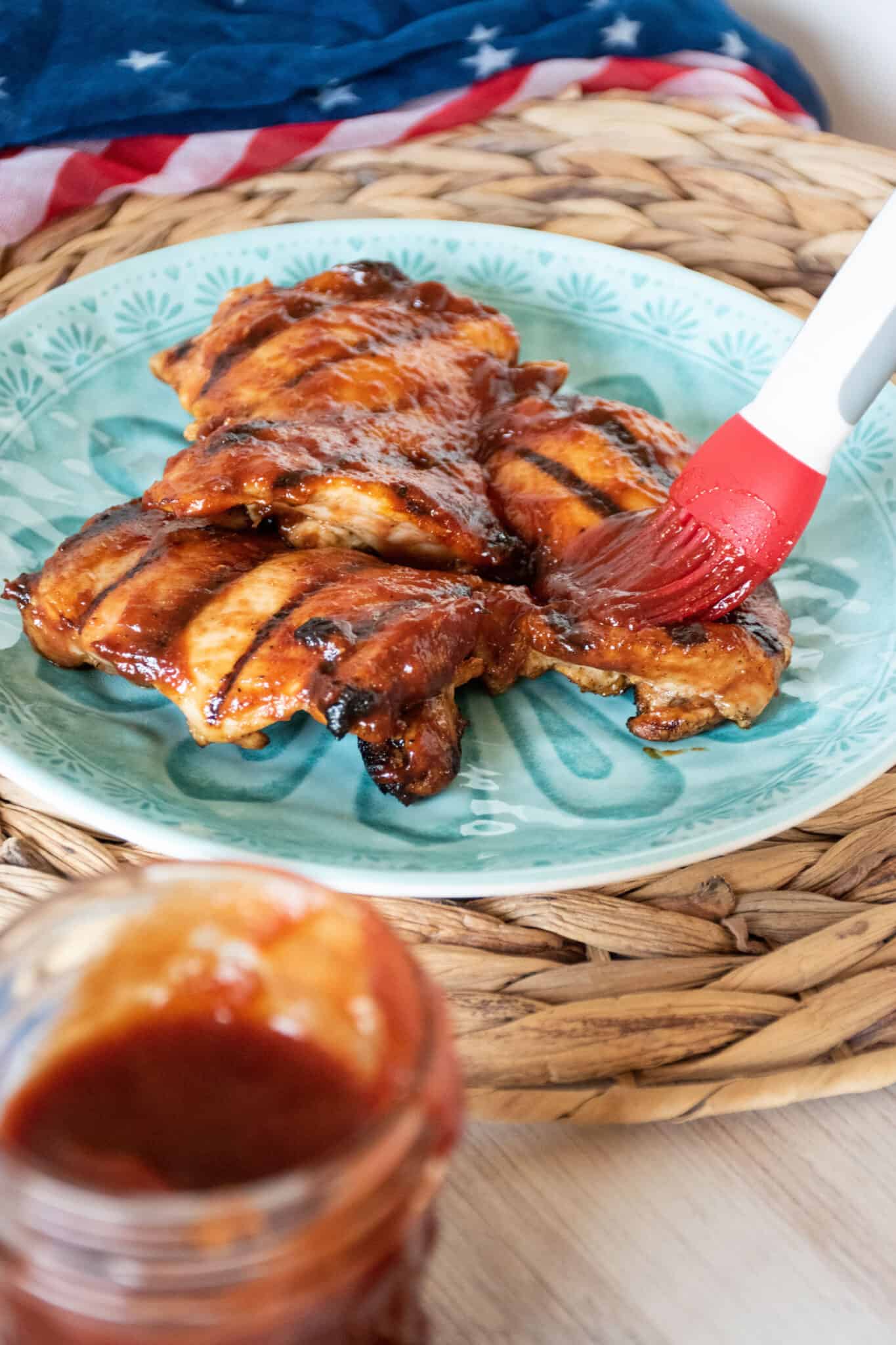 Plate of grilled chicken with BBQ sauce being brushed on