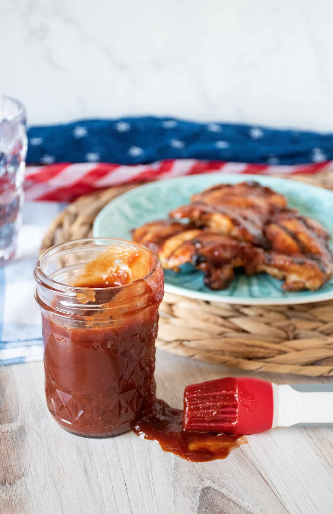 BBQ sauce in a mason jar with grilled chicken on a plate in the background.