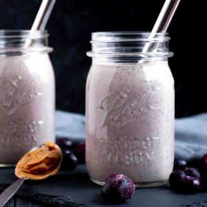 Berry smoothie in a mason jar, with frozen berries scattered around the outside, and a spoon with peanut butter on it.