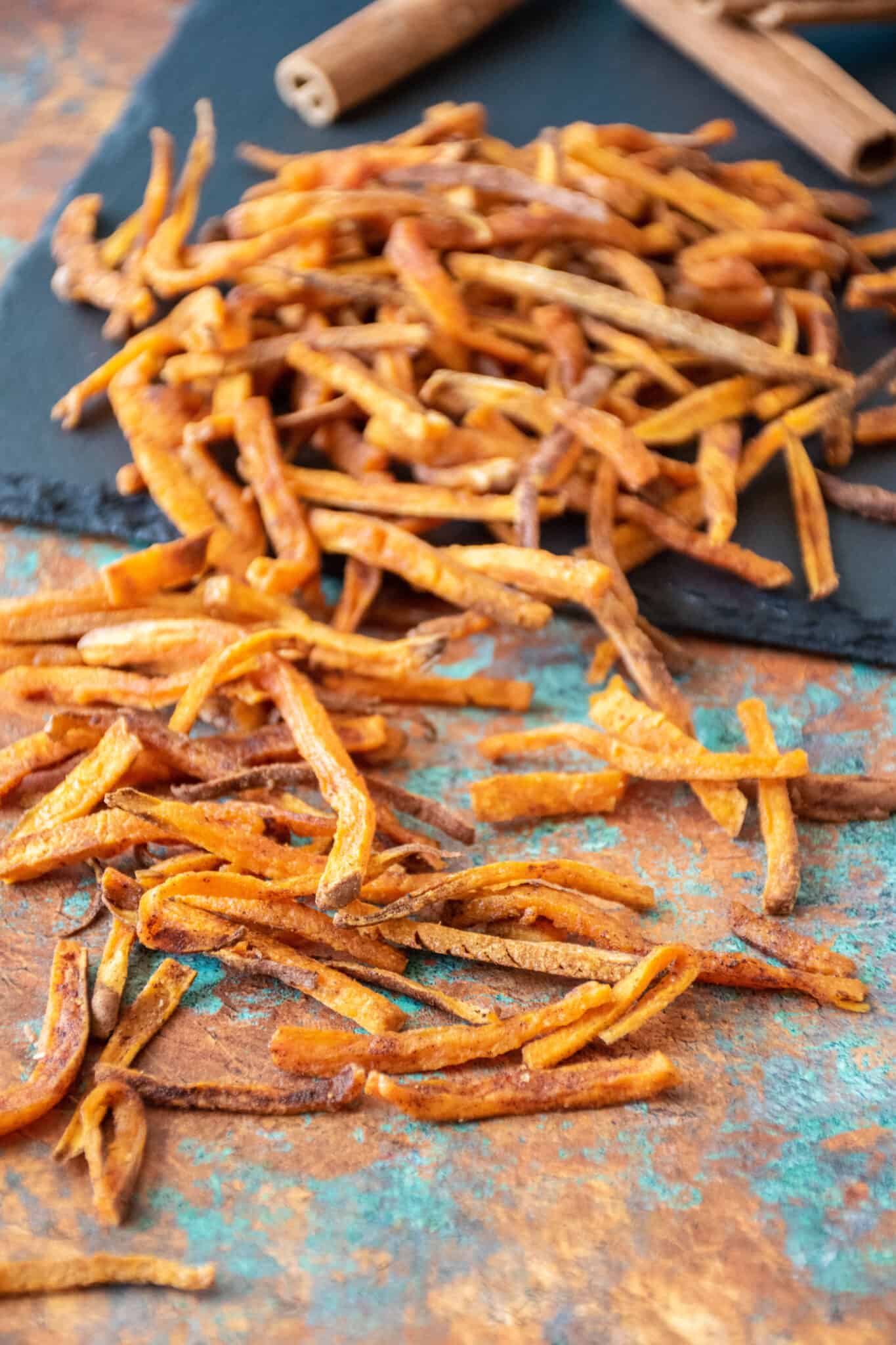 A pile of sweet potato fries, spilling off of a slate plate.