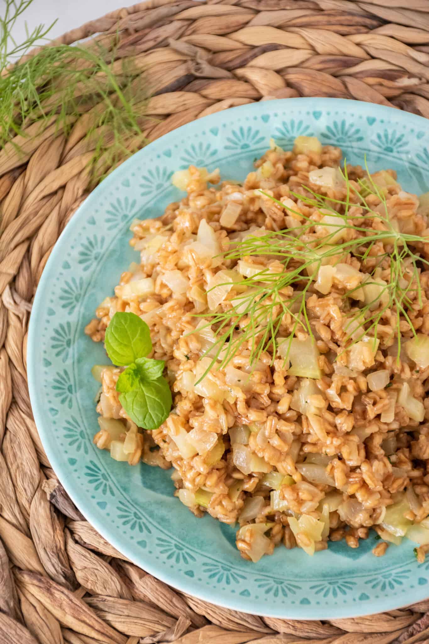 A plate with farro pilaf on it, ready for serving, garnished with fresh mint and a fennel frond.