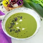 A bowl of celery soup, garnished with microgreens, black sesame seeds and yogurt. A side salad is in the background.
