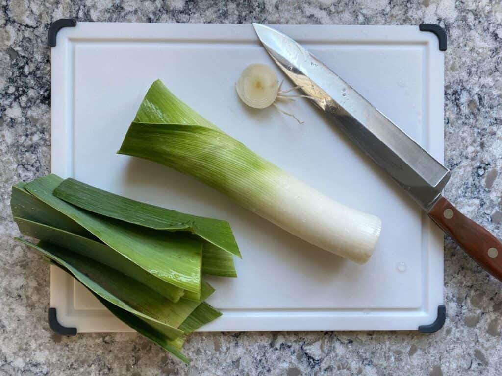A leek on a cutting board with the tops and bottom cut off.