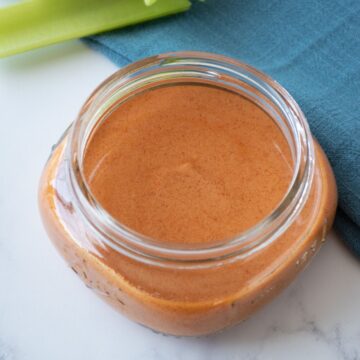 Buffalo sauce in a small jar, with celery sticks in the background.