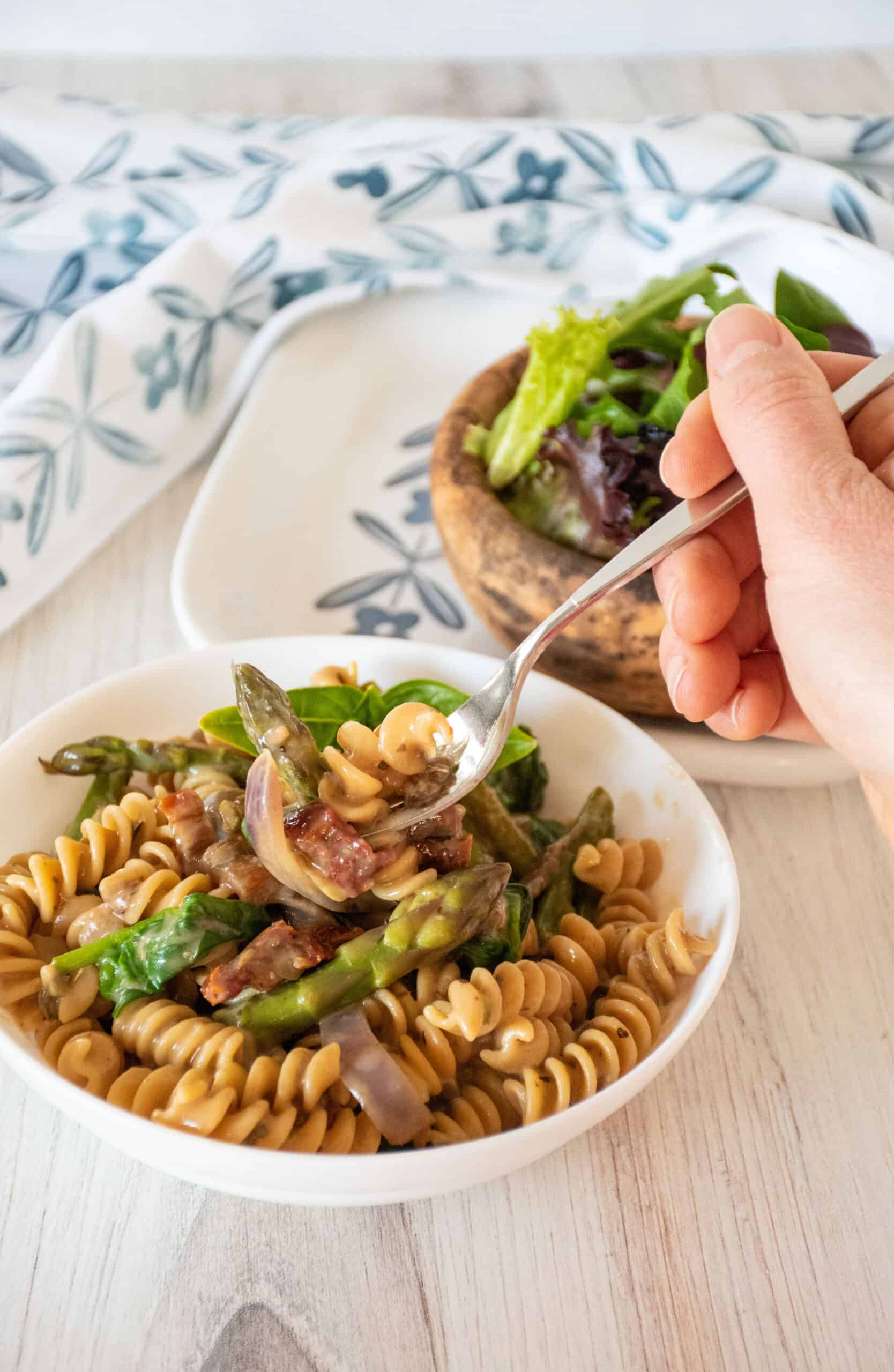 A fork with rotini pasta and veggies on it being lifted out of a bowl of the pasta.