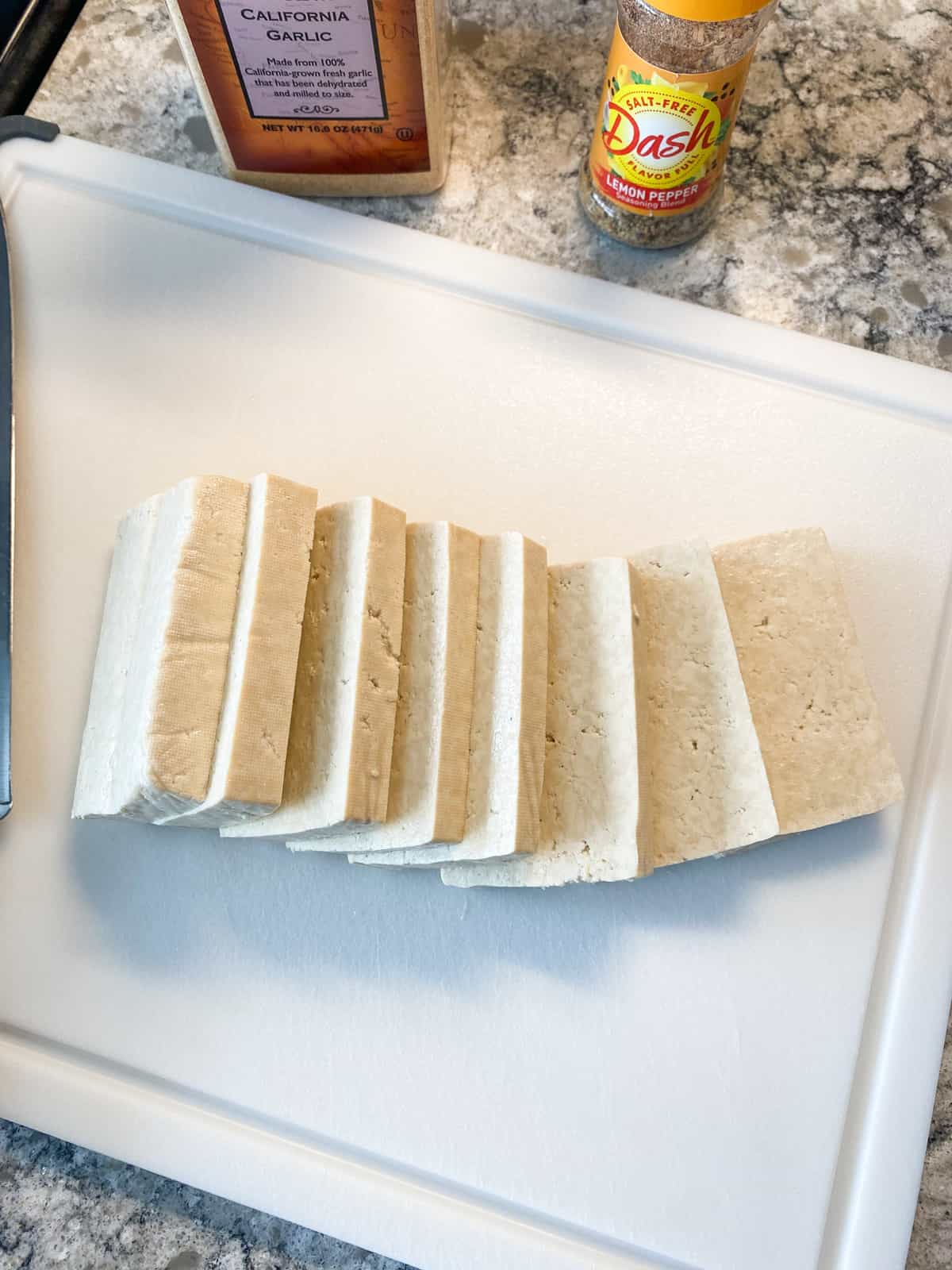Block of tofu, sliced on a cutting board.