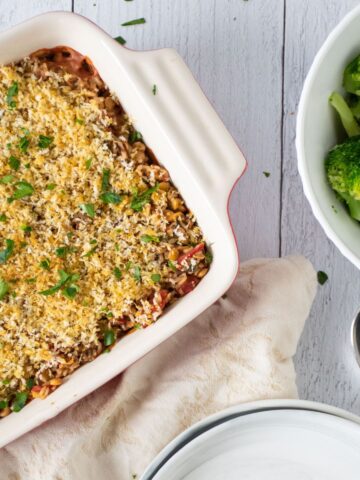 Overhead image of a casserole in a casserole dish, with a bowl of steamed broccoli nearby.