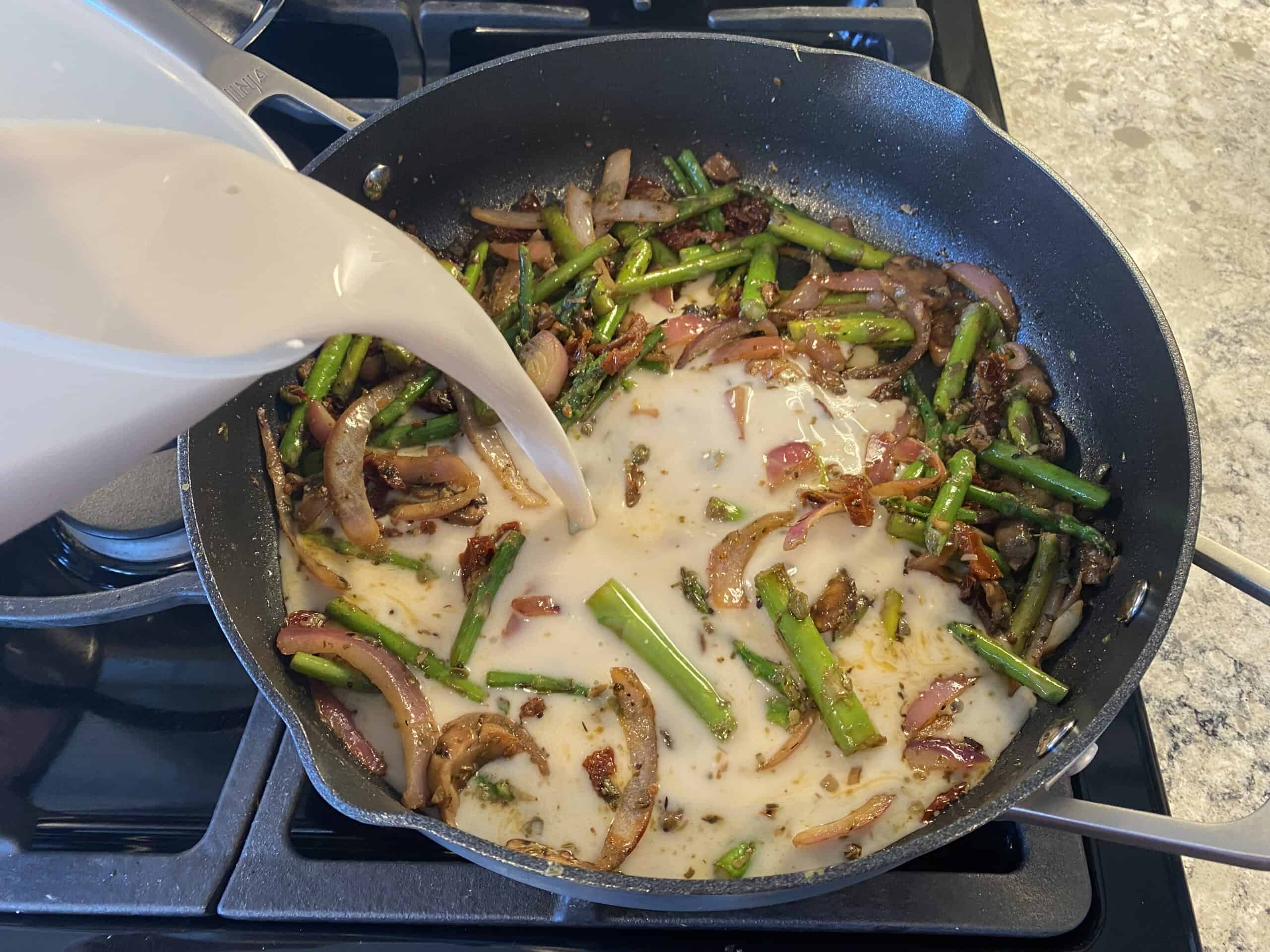 Pouring cashew milk into a pan of sauteed vegetables.