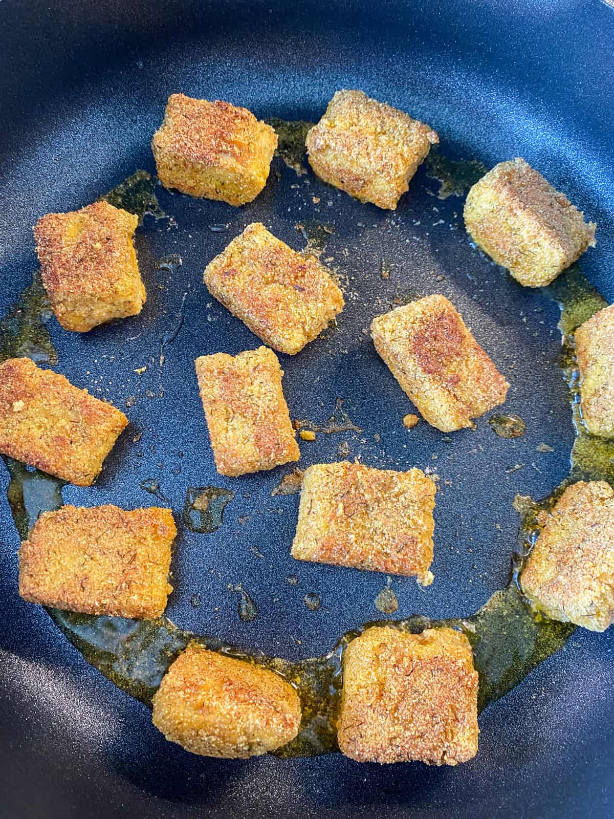 Buffalo tempeh cooking in a skillet, browned on the top.