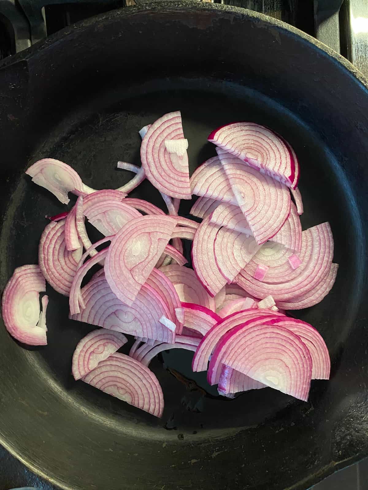 Sliced, raw red onions in a skillet, ready for caramelization.