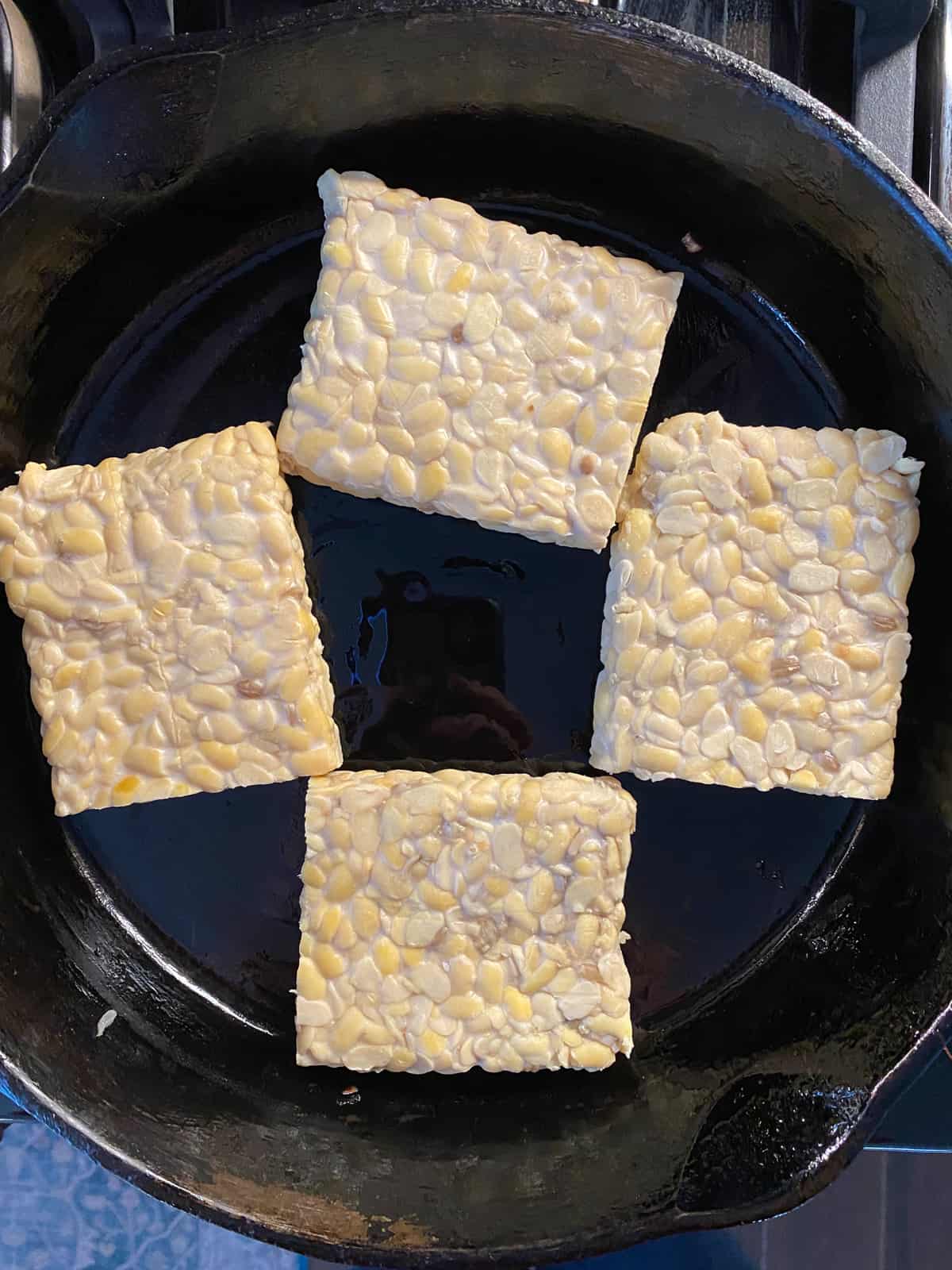 Uncooked tempeh in a skillet, being sauteed.