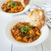 Two bowls of ratatouille with crusty bread on the side.
