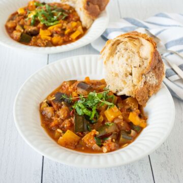 Two bowls of ratatouille with crusty bread on the side.