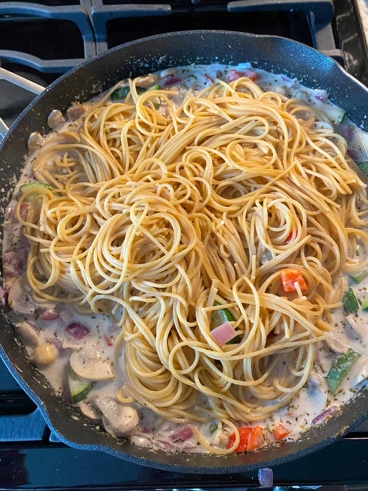 Cooked pasta added to pan with sauteed vegetables and sauce.