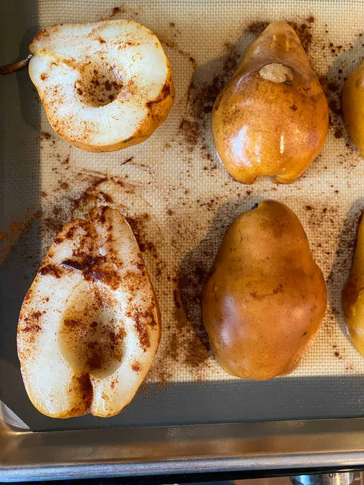 Halved pears on a baking sheet, some cut side down, and some are cut side up.