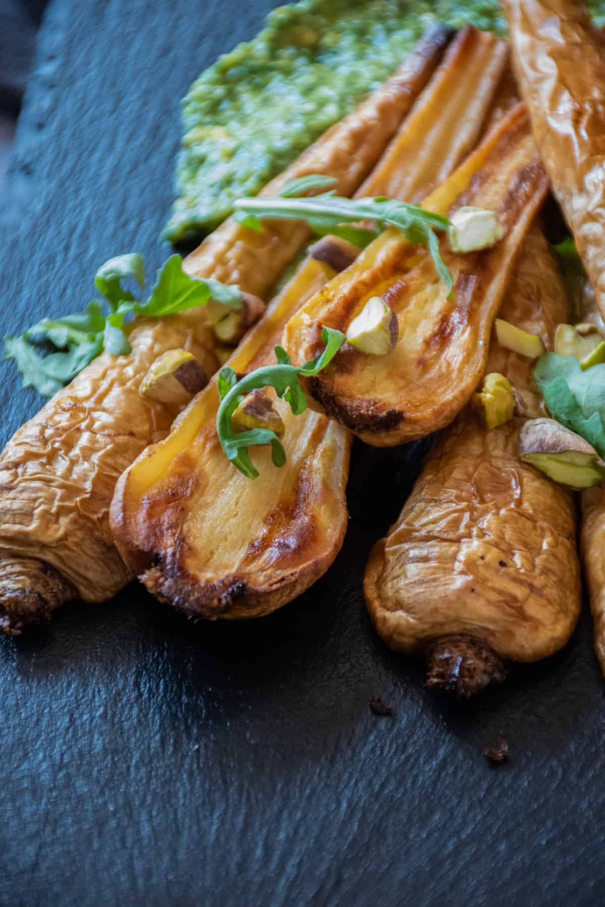 Roasted, halved parsnips, on a platter, with pesto sauce smeared under them.