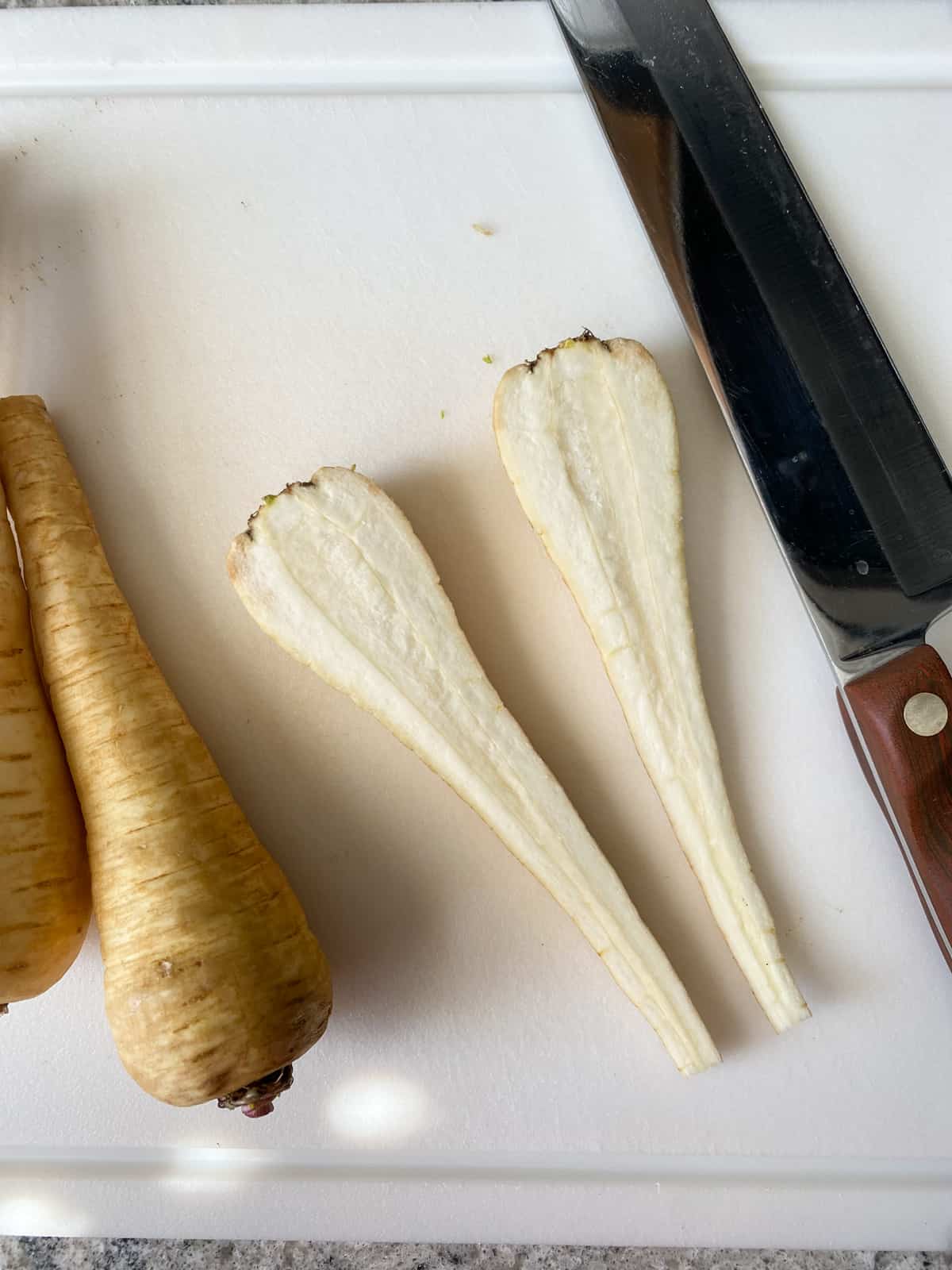 One parsnip, halved lengthwise, on a cutting board beside a chef knife.