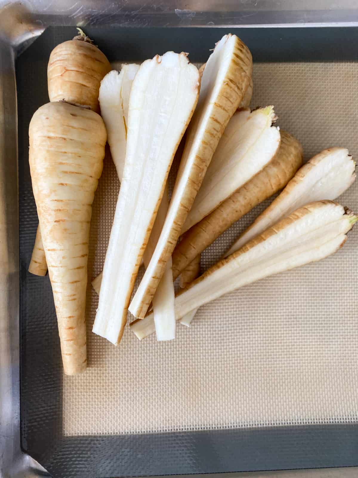 Halved raw parsnips in a pile on a cutting board.
