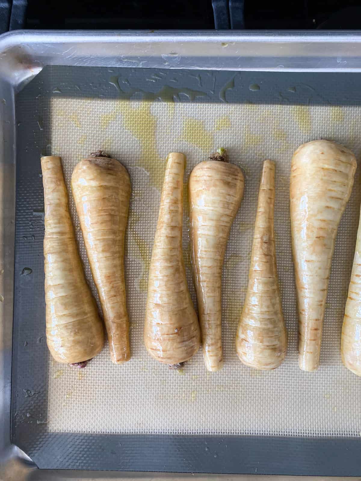 Raw parsnips, halved, tossed with oil on a baking sheet.
