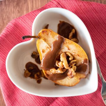 Half of a baked pear in a dish, drizzled with chocolate sauce and toasted walnuts.
