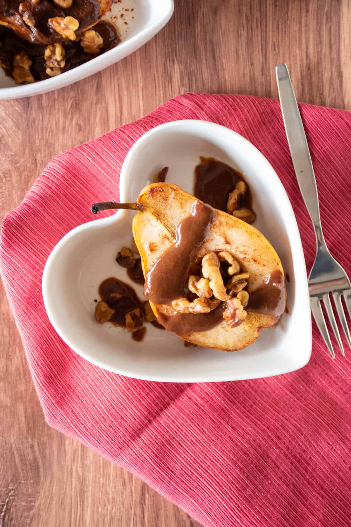 Half of a baked pear in a dish, drizzled with chocolate sauce and toasted walnuts.