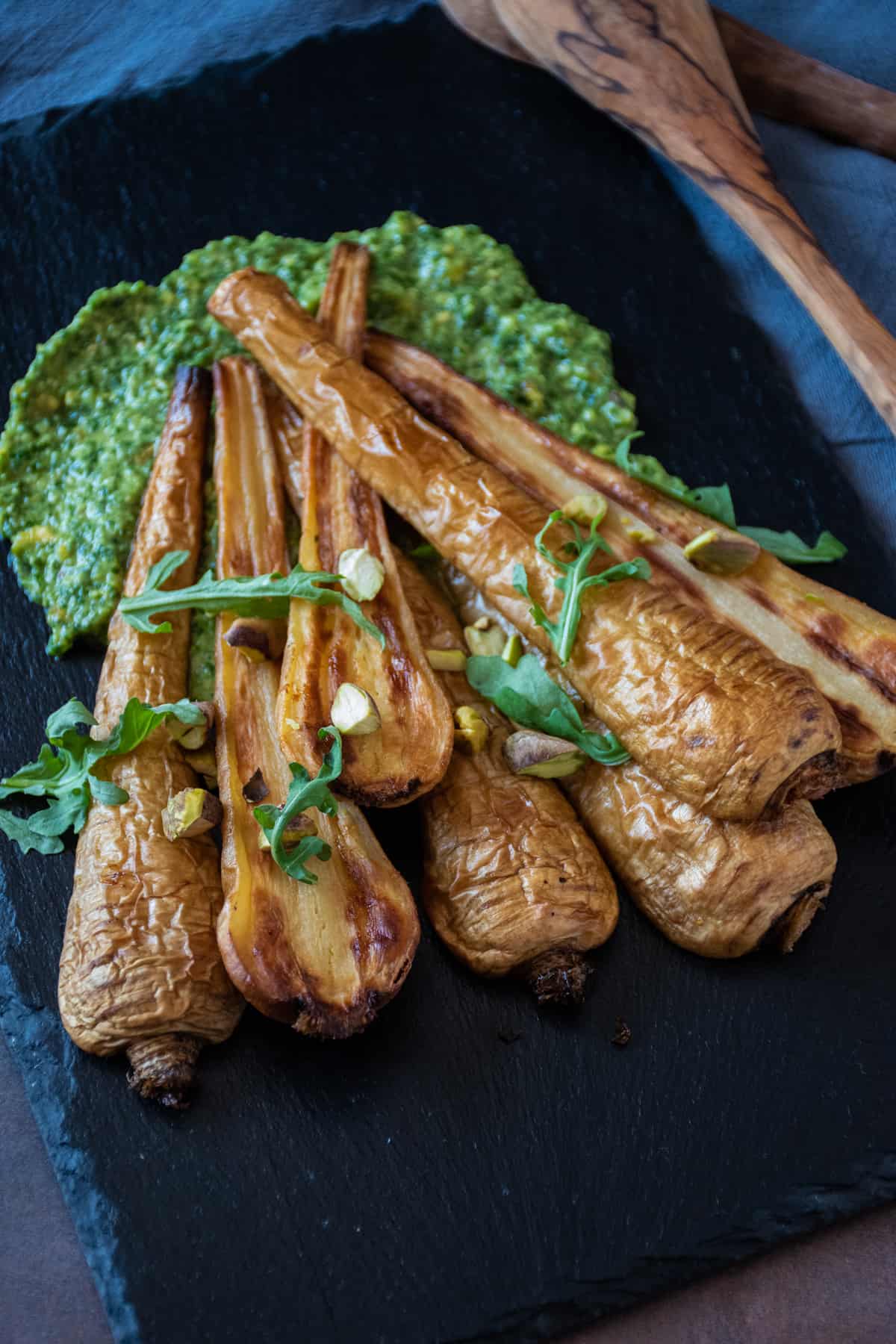 Roasted, halved parsnips, on a platter, with pesto sauce smeared under them.