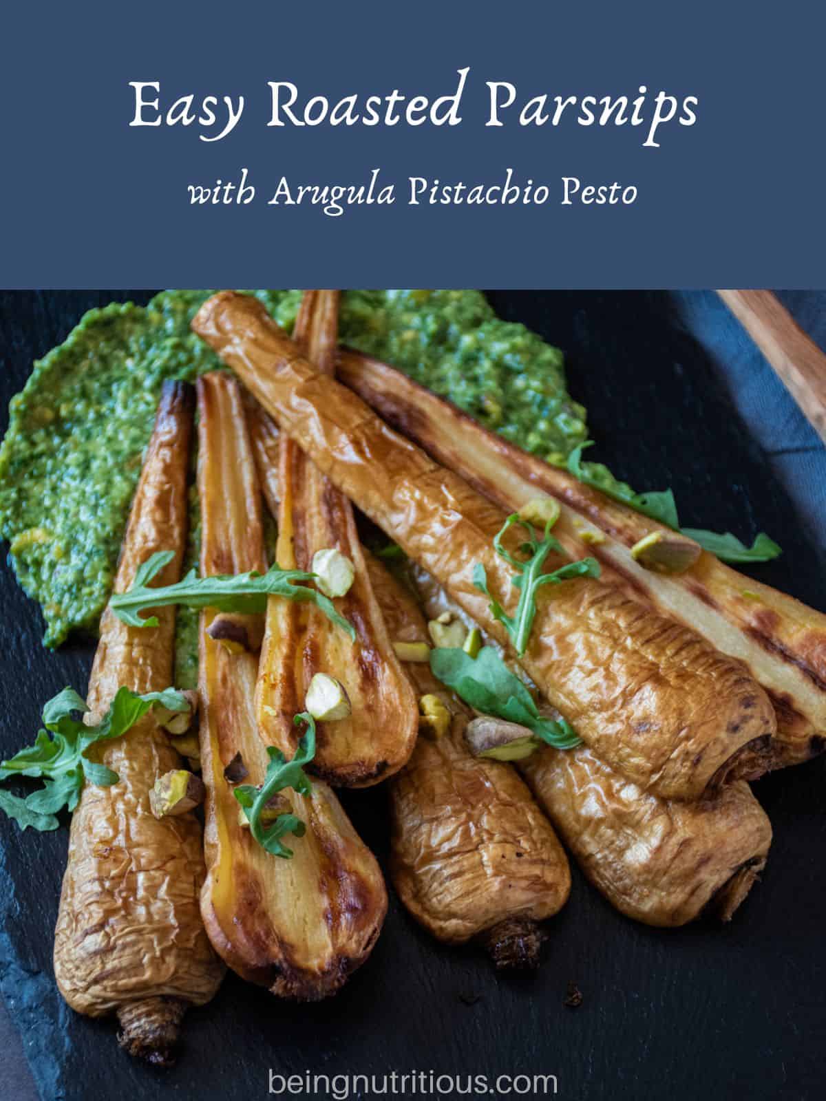 Roasted, halved parsnips, on a platter, with pesto sauce smeared under them. Text overlay: Easy Roasted Parsnips with Arugula Pistachio Pesto.