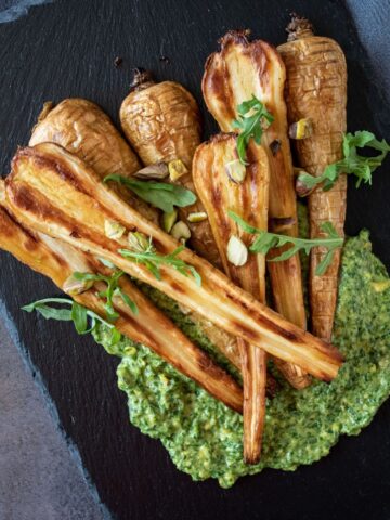 Roasted, halved parsnips, on a platter, with pesto sauce smeared under them.